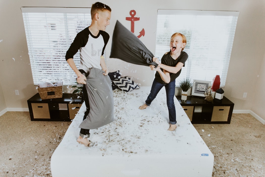 Two children pillow-fighting on a white bed