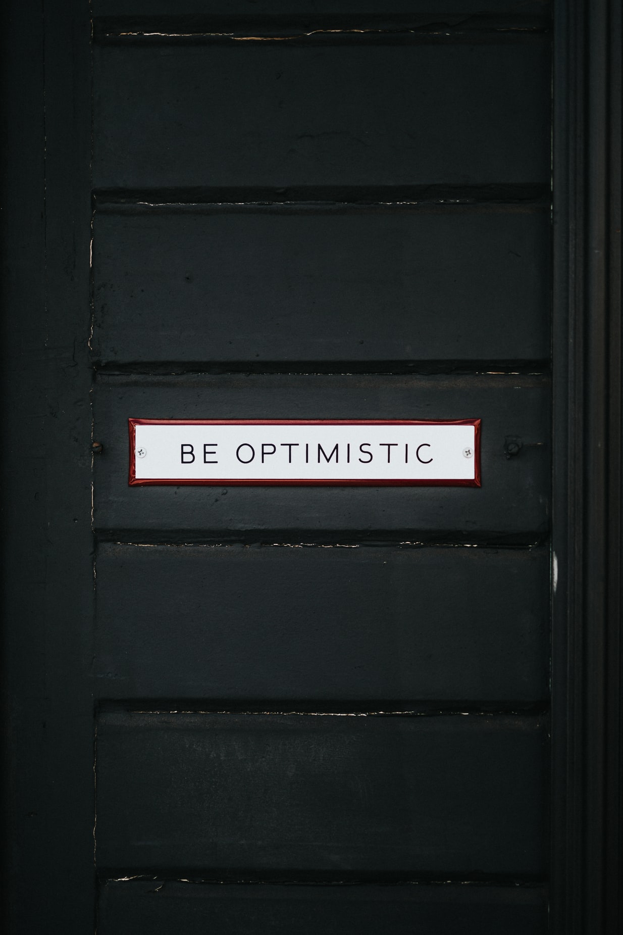 A black door with the inscription; "Be Optimistic".
